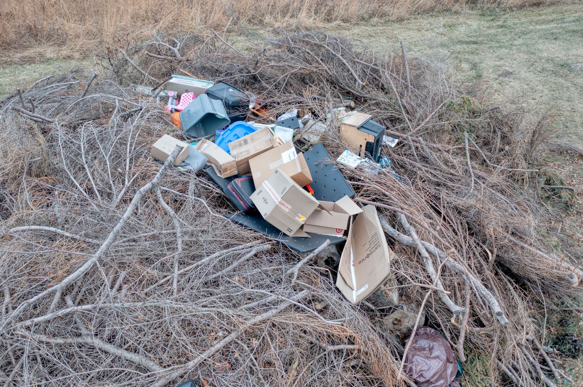 High angle view of boxes and garbage discarded among dry branches in an outdoor setting.